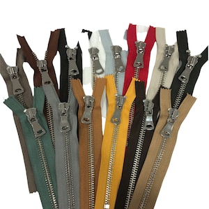 Könnte beinhalten: Sortiment an Metallreißverschlüssen in verschiedenen Farben, darunter Rot, Gelb, Grün, Braun, Grau und Beige. Die Reißverschlüsse sind alle geschlossen und haben eine silberne Oberfläche.