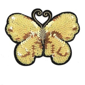May include: A decorative butterfly patch with gold sequins and brown accents. The butterfly has a black outline and a detailed design, perfect for embellishing clothing or accessories.