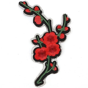 Op de afbeelding: Rode geborduurde bloemenpatch met groene bladeren en een zwarte achtergrond. De patch is omgeven door heldere strass steentjes.