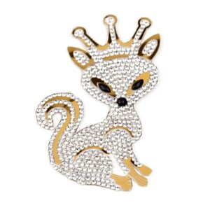 May include: A white fox wearing a gold crown, covered in rhinestones. The fox is sitting with its tail curled behind it.