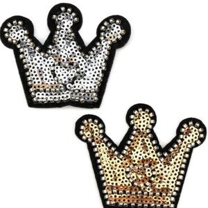 May include: Two crown-shaped patches. One is silver with a black border, and the other is gold with a black border. Both patches are covered in sequins, giving them a sparkling appearance. The crowns have three rounded points.