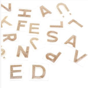 May include: A set of gold rhinestone letters, including A, D, E, F, H, J, K, L, N, P, R, S, T, U, V, and a question mark. The letters are on a white background.
