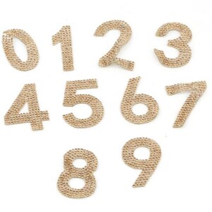 May include: Ten gold rhinestone numbers, 0 through 9, on a white background.