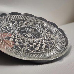 May include: Clear glass serving tray with a divided design. The tray features a diamond pattern and a scalloped edge. The center has a starburst design. This vintage serving dish is perfect for appetizers or snacks.