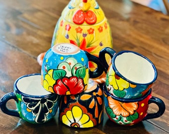 May include: Set of four colorful ceramic mugs with floral designs. The mugs have blue rims and handles. One mug has the text "Lead Free Mex" on the bottom.