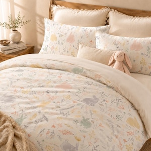 May include: A bed with a cream-colored duvet cover and pillowcases. The bedding features a floral and bunny pattern in pastel colors. A plush bunny toy sits on the bed, adding a touch of whimsy to the bedroom decor.