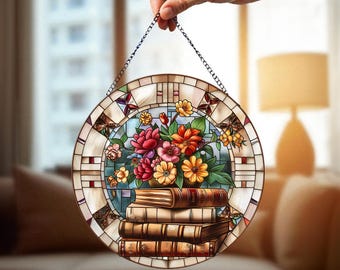 May include: Round stained glass panel featuring a floral arrangement of red, orange, and yellow flowers above a stack of books. The panel has a decorative border and is suspended by a chain.
