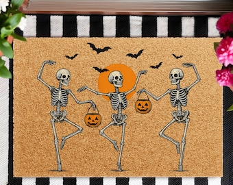 May include: Halloween-themed doormat featuring three dancing skeletons holding jack-o'-lanterns. The skeletons are set against a tan background with an orange sun and black bats. The mat has a black and white striped border.