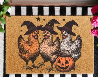 May include: A Halloween-themed doormat featuring three chickens wearing witch hats and a jack-o'-lantern. The chickens are in shades of orange, brown, and white, with black hats adorned with gold stars. The mat is made of a tan material.