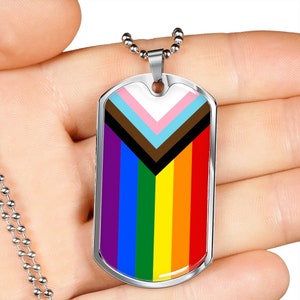 May include: A silver dog tag necklace with a rainbow pride flag and a black, brown, light blue, pink, and white chevron design.