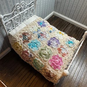 May include: A white metal bed frame with a crocheted bedspread in shades of pink, purple, blue, green, and yellow. The bedspread has a floral pattern.