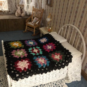 May include: A black crochet granny square throw with colorful accents on a white bed with a white crocheted bedspread.