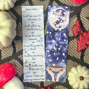 May include: Amas Veritas bookmark with a blue background and a moon with white petals falling from it. The text on the bookmark reads: "He will hear my call a mile away... He will whistle my favorite song... He can ride a pony backwards... He can flip pancakes in the air... He will be marvelously kind... And his favorite shape will be a star... And he'll have one green eye and one blue."