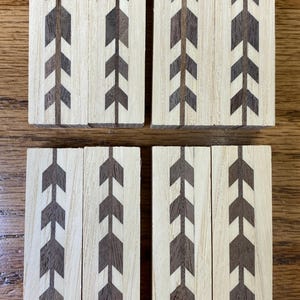 May include: Eight rectangular wooden blocks with a light wood grain background. Each block features a dark brown arrow design. The arrows are arranged in a vertical pattern, creating a repeating motif. The blocks are arranged in two rows of four.