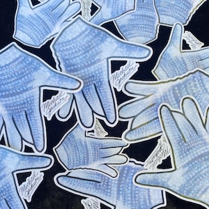 May include: A collection of light blue and white glove stickers with a textured pattern. Each sticker has the handwritten text "Michael Jackson" in black. The stickers are arranged on a black background.