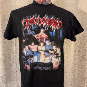 Puede incluir: Camiseta negra con un diseño gráfico que presenta la palabra "Tankard" en rojo y blanco, sobre una ilustración de temática zombi. El texto "Zombie Attack" está en la parte inferior. La camiseta se muestra en un maniquí.