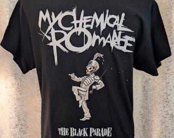 May include: A black short-sleeve t-shirt featuring the white text My Chemical Romance at the top and The Black Parade at the bottom. In the center is a graphic of a skeleton figure dressed in a white marching band uniform with a feathered hat.