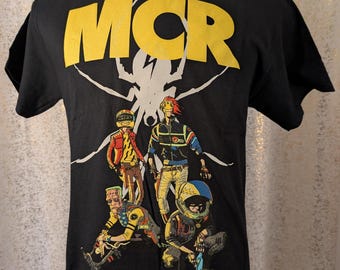 May include: Black t-shirt with the yellow text "MCR" above a white spiderweb design. Below the text is a colorful graphic of four figures in futuristic outfits. The figures are in various poses.