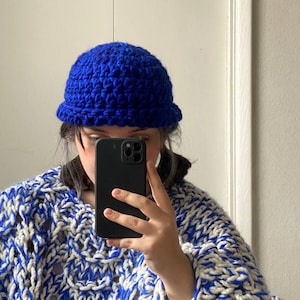 Op de afbeelding: Een persoon draagt ​​een blauwe gebreide beanie-muts en een wit-blauwe grove gebreide trui.