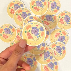 May include: A collection of colorful cell stickers with a cartoon-like design. Each sticker features a yellow circle with a smiling face and a detailed illustration of a cell's internal components.