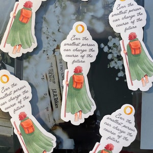 May include: A set of five stickers featuring a cartoon character with red hair and a green cloak holding a staff. The stickers have a white background with a gold ring and the text "Even the smallest person can change the course of the future".