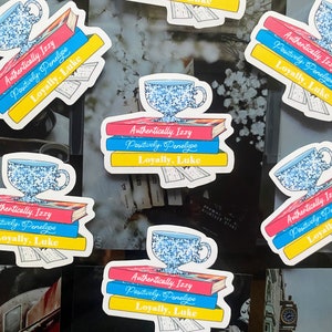 May include: A set of five stickers featuring a blue and white teacup with a stack of three books. The books have the text "Authentically Izzy", "Positively Penelope", and "Loyally, Luke" in a colorful font.