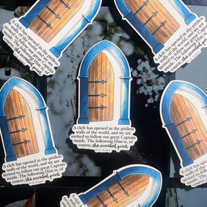 May include: Several stickers depicting an arched doorway with a wooden door and blue detailing. The stickers feature a quote by C.S. Lewis: "A cleft has opened in the pitiless walls of the world..."