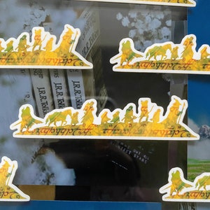 May include: A set of nine yellow and white stickers featuring a silhouette of the Fellowship of the Ring from the Lord of the Rings book series. The stickers are printed with the text "The Fellowship of the Ring" in Elvish script.