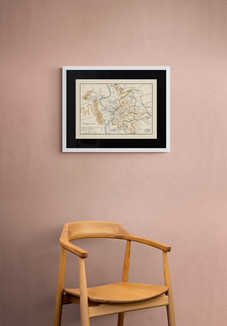 May include: A framed vintage map of the city of Ancient Rome, with a black frame and a white mount, hanging on a pale pink wall. A wooden chair is in the foreground.