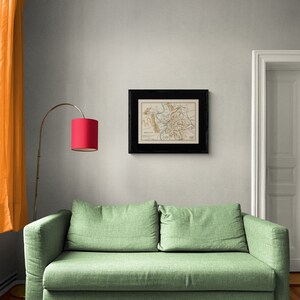 May include: A green fabric sofa with two cushions sits in a room with a framed map on the wall and a red lamp on a stand.