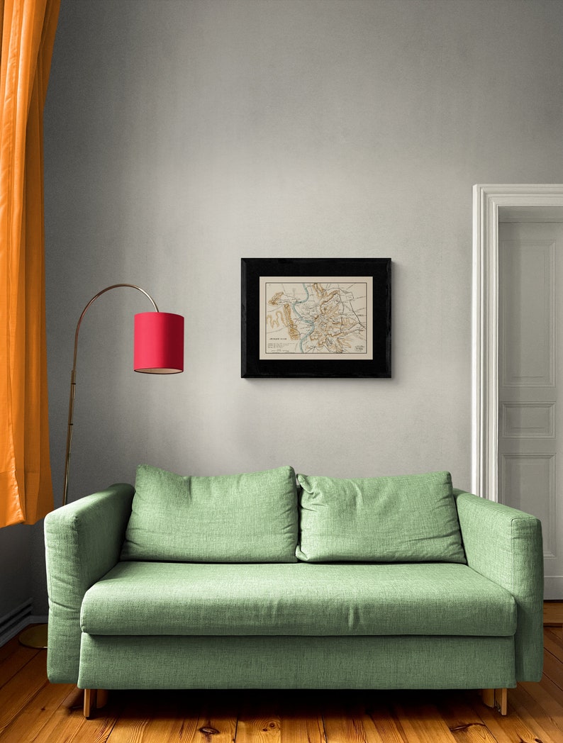 May include: A green fabric sofa with two cushions sits in a room with a framed map on the wall and a red lamp on a stand.