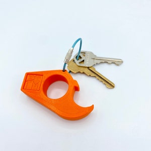 May include: Orange plastic keychain with a bottle opener and a ring. The keychain has a small logo that says "KM". The keychain is attached to two keys with a blue cord.