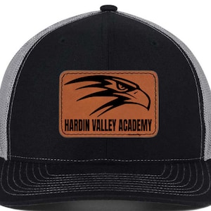 Könnte beinhalten: Schwarze und graue Trucker-Kappe mit einem braunen Leder-Patch, auf dem ein schwarzer Adler und der Text "Hardin Valley Academy" zu sehen sind.