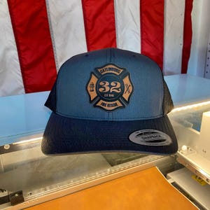 May include: A blue and black trucker hat with a black and orange embroidered patch that says "Gatlinburg Fire Rescue Est. 1940" and a number "32" inside a red cross.