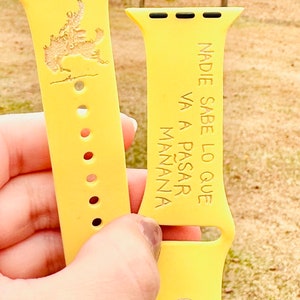 May include: Two yellow watch bands are held up. One band features a detailed engraving of a cowboy on a horse. The other band has the Spanish text "NADIE SABE LO QUE VA A PASAR MAÑANA".
