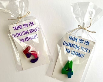 May include: Two clear cellophane bags with thank you tags. The tags have purple and blue text that says "Thank you for celebrating Kayla's 5th birthday!" and "Thank you for celebrating Tyler's 4th birthday!"  Each bag contains a wooden number, one is a red and purple 5 and the other is a green 4.