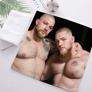 May include: Two shirtless men with beards and tattoos are shown in a close-up photo. The man on the left has a beard and a tattoo on his chest. The man on the right has a beard and a tattoo on his chest and shoulder.