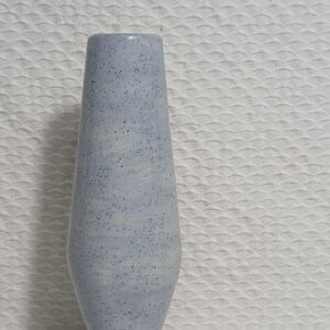 Pode incluir: Um vaso de cerâmica azul claro com acabamento salpicado. O vaso tem um pescoço estreito e uma base larga.