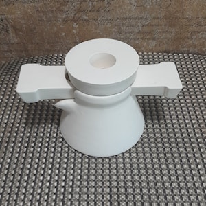 Könnte beinhalten: Weiße Kaffeekanne aus Keramik mit einem Holzgriff. Die Kanne steht auf einer gemusterten Oberfläche.