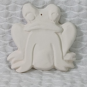 Könnte beinhalten: Weiße Keramik-Froschfigur mit glatter, abgerundeter Oberfläche. Der Frosch hat ein Loch oben auf dem Kopf, was darauf hindeutet, dass es sich um einen hängenden Anhänger handeln könnte.