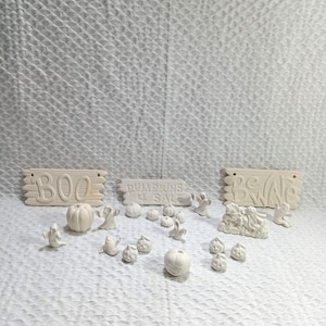 Może przedstawiać: Zestaw białych ceramicznych dekoracji halloweenowych, w tym tabliczki z napisami "BOO", "PUMPKINS EL SAL" i "BEWARE", a także różne figurki dyni i duchów.
