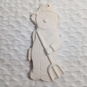 Op de afbeelding: Witte keramische ornament van een persoon die een hark vasthoudt. De ornament is leeg en klaar om te worden beschilderd.