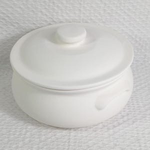 May include: A white ceramic casserole dish with a lid. The dish has a rounded body with two small handles and a lid with a small knob. The dish is sitting on a white textured surface.