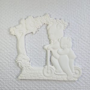 Op de afbeelding: Witte wanddecoratie met twee teddyberen, één op een scooter, de ander knuffelend. Links een boom met vogels. Het stuk is gemaakt van een solide, glad materiaal. Afmetingen in centimeters.