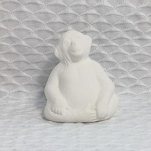 Könnte beinhalten: Weiße Keramikfigur eines Affen, der mit gekreuzten Beinen sitzt. Der Affe hat einen lächelnden Ausdruck und befindet sich in einer entspannten Pose.