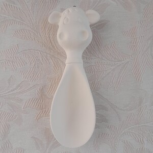 May include: A white ceramic spoon with a cow head design. The spoon features a cow's face at the top, with ears and a rounded snout. The spoon's bowl is teardrop-shaped. The item is unpainted and ready for customization.