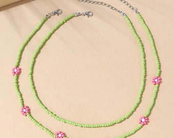 Puede incluir: Dos collares superpuestos con cuentas verdes y detalles de flores rosas. Los collares están hechos de cuentas pequeñas y tienen un aspecto delicado.