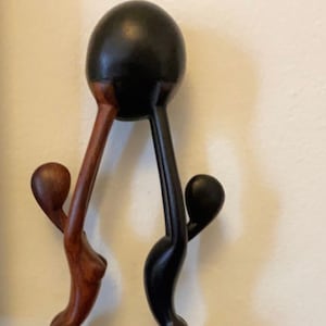 Pode incluir: Uma escultura de madeira de duas figuras segurando uma esfera preta acima de suas cabe&ccedil;as. A figura &agrave; esquerda &eacute; marrom e a figura &agrave; direita &eacute; preta.