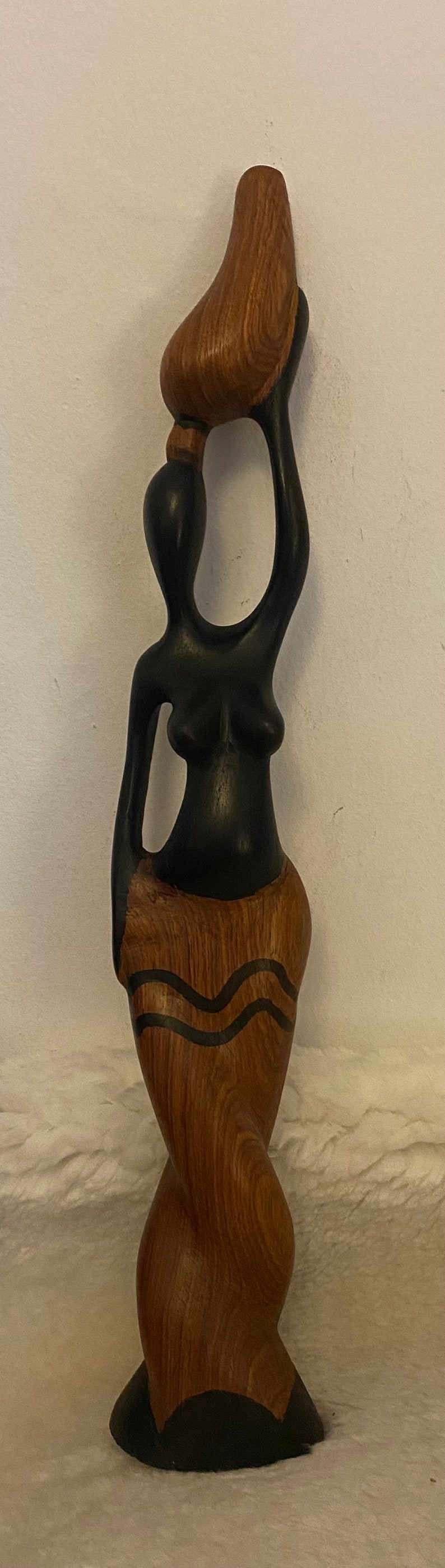 Pode incluir: Escultura de madeira de uma mulher a carregar um pote na cabe&ccedil;a. A escultura &eacute; pintada de preto e castanho com um padr&atilde;o de gr&atilde;o de madeira.