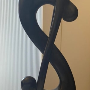 Pode incluir: Uma escultura de madeira preta de uma figura abstrata com uma base arredondada. A escultura tem a forma de um s&iacute;mbolo de infinito.
